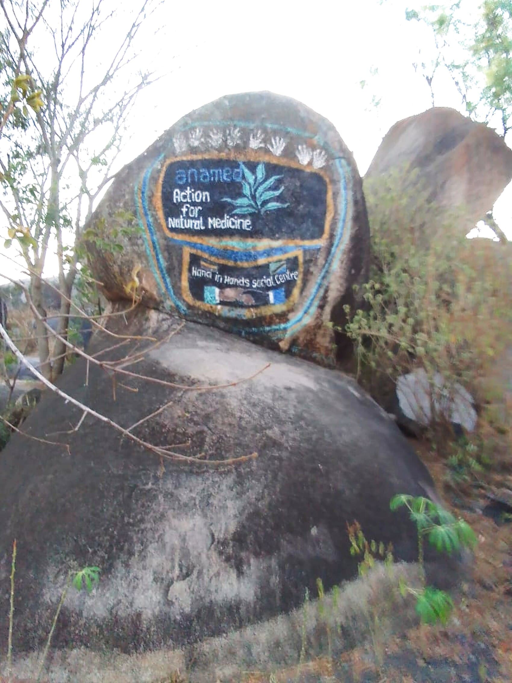 Granitfelsen auf dem Gelände in Mwanza, bemalt mit dem anamed-Zeichen „Action for Natural Medicine“ und dem Schriftzug „Hand in Hands Social Centre“